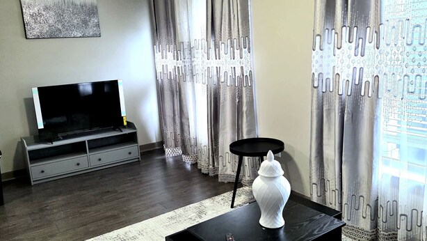 A living room with a flat-screen TV, a ceiling fan, a black coffee table with a white vase, and grey curtains. - Prime 1-bedroom apartment in Uptown Charlotte with Pool and gym (Charlotte)