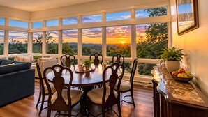 A dining area with a large window overlooking a scenic landscape, wooden chairs, a table with a vase, and a bowl of fruit on a marble counter. - Work & Relax Retreat, Pool, Wifi, Stocked Kitchen (Nashville)