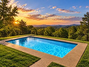 Piscina rectangular con agua cristalina azul, rodeada de césped cuidado y una valla de metal negro.