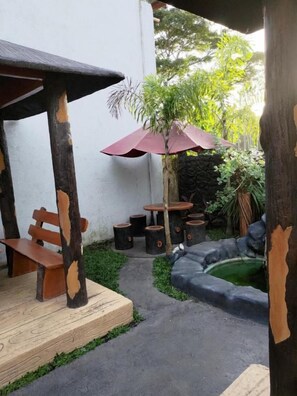 An outdoor seating area with wooden benches and tables, surrounded by greenery and a small pond. - JLF Inn (Daraga)