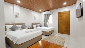 A hotel room with two beds, a wooden ceiling, a TV, and a door.