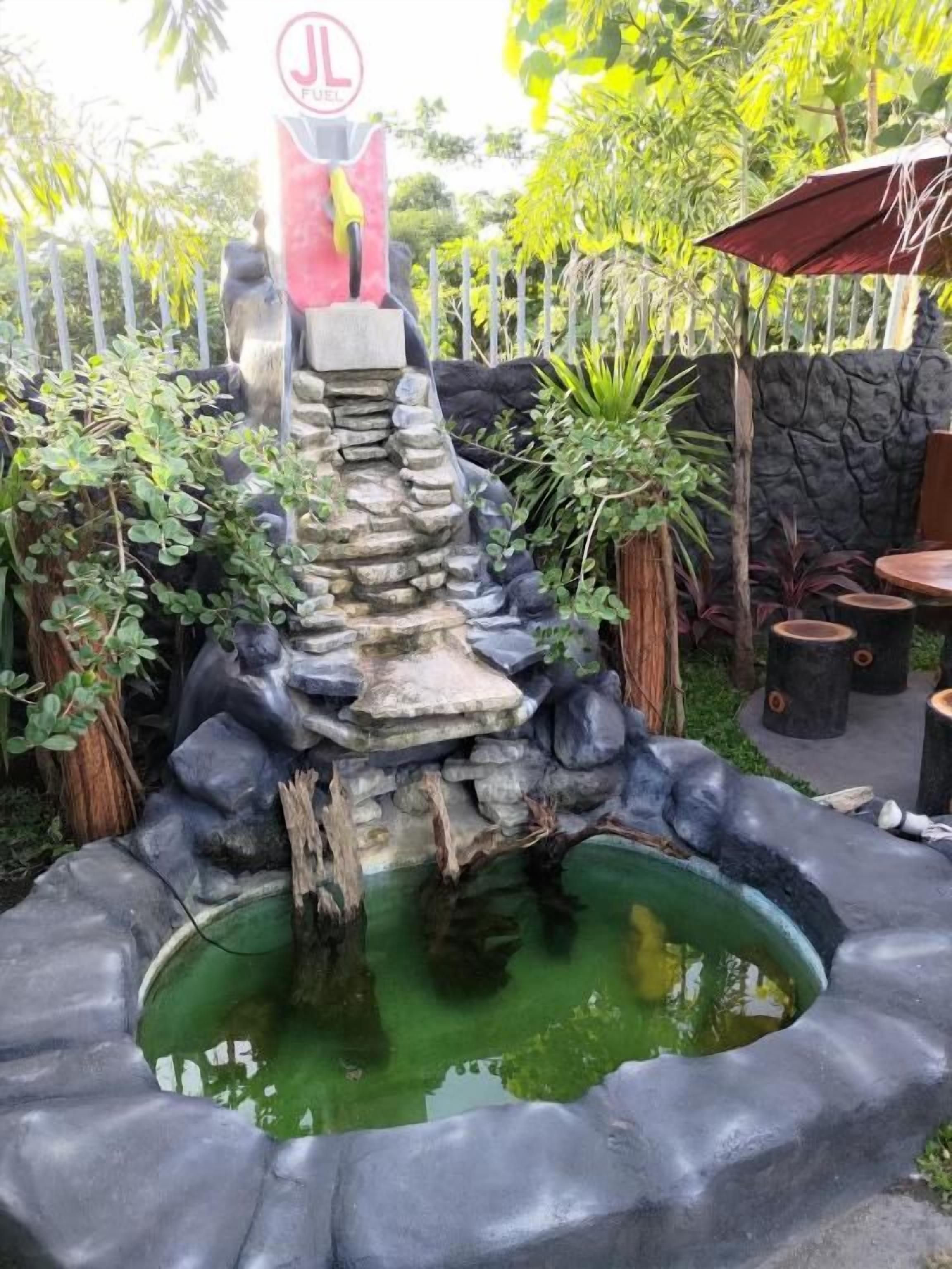 Un jardín con una cascada de rocas, un estanque y una zona de estar con sombrilla.