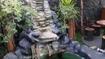 Un jardín con una cascada de rocas, un estanque y una zona de estar con sombrilla.