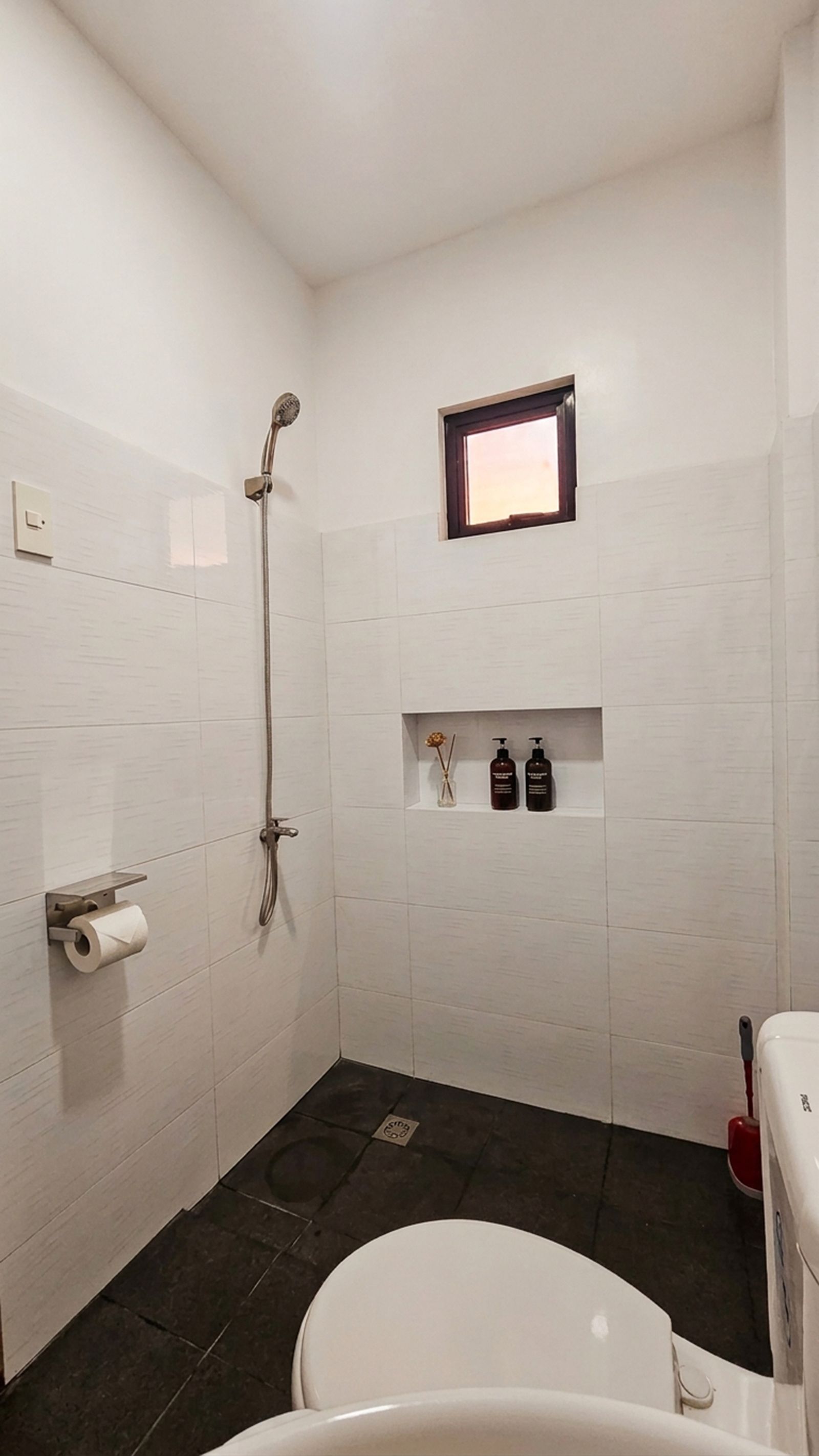 Un baño con ducha, inodoro y un estante con artículos de aseo.