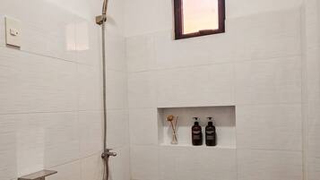 Un baño con ducha, inodoro y un estante con artículos de aseo.