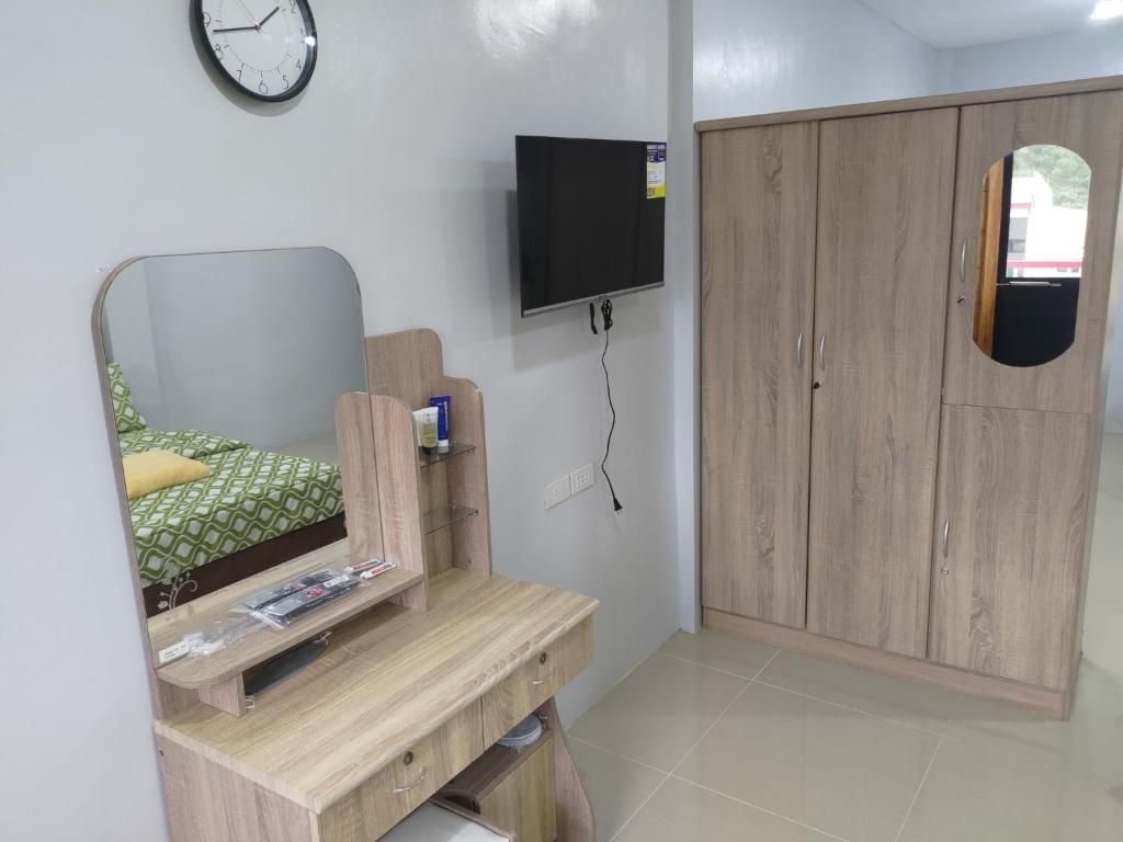 Quarto com cama, escrivaninha de madeira, TV fixada na parede e guarda-roupa.