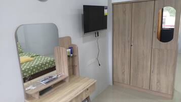 Quarto com cama, escrivaninha de madeira, TV fixada na parede e guarda-roupa.