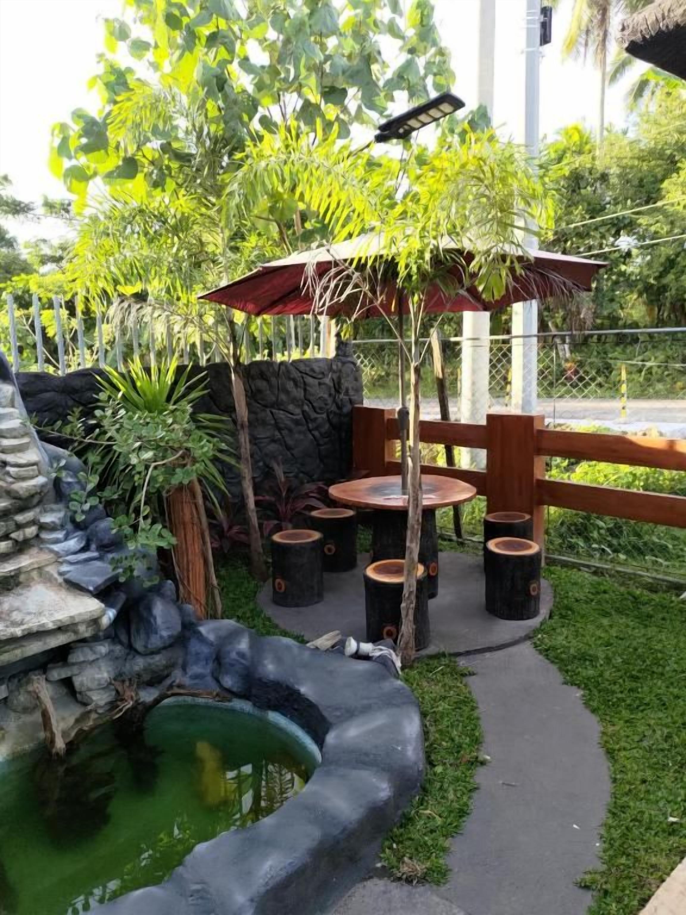 Un jardín con estanque, asientos de madera y una sombrilla de paja.