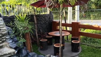 Un jardín con estanque, asientos de madera y una sombrilla de paja.