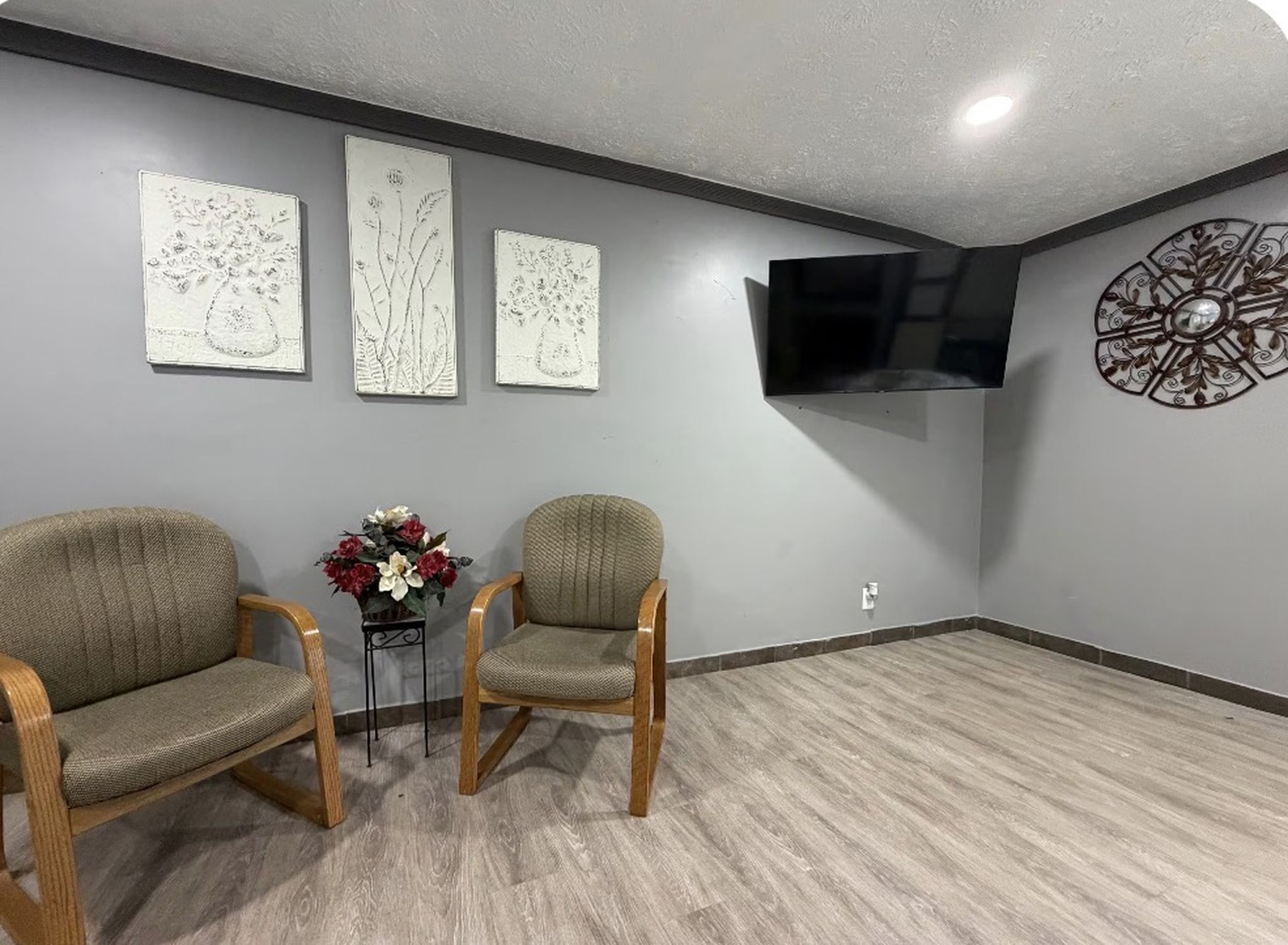 Une pièce comprenant deux chaises en bois, une petite table ornée d’un vase de fleurs et trois œuvres d’art accrochées au mur.
