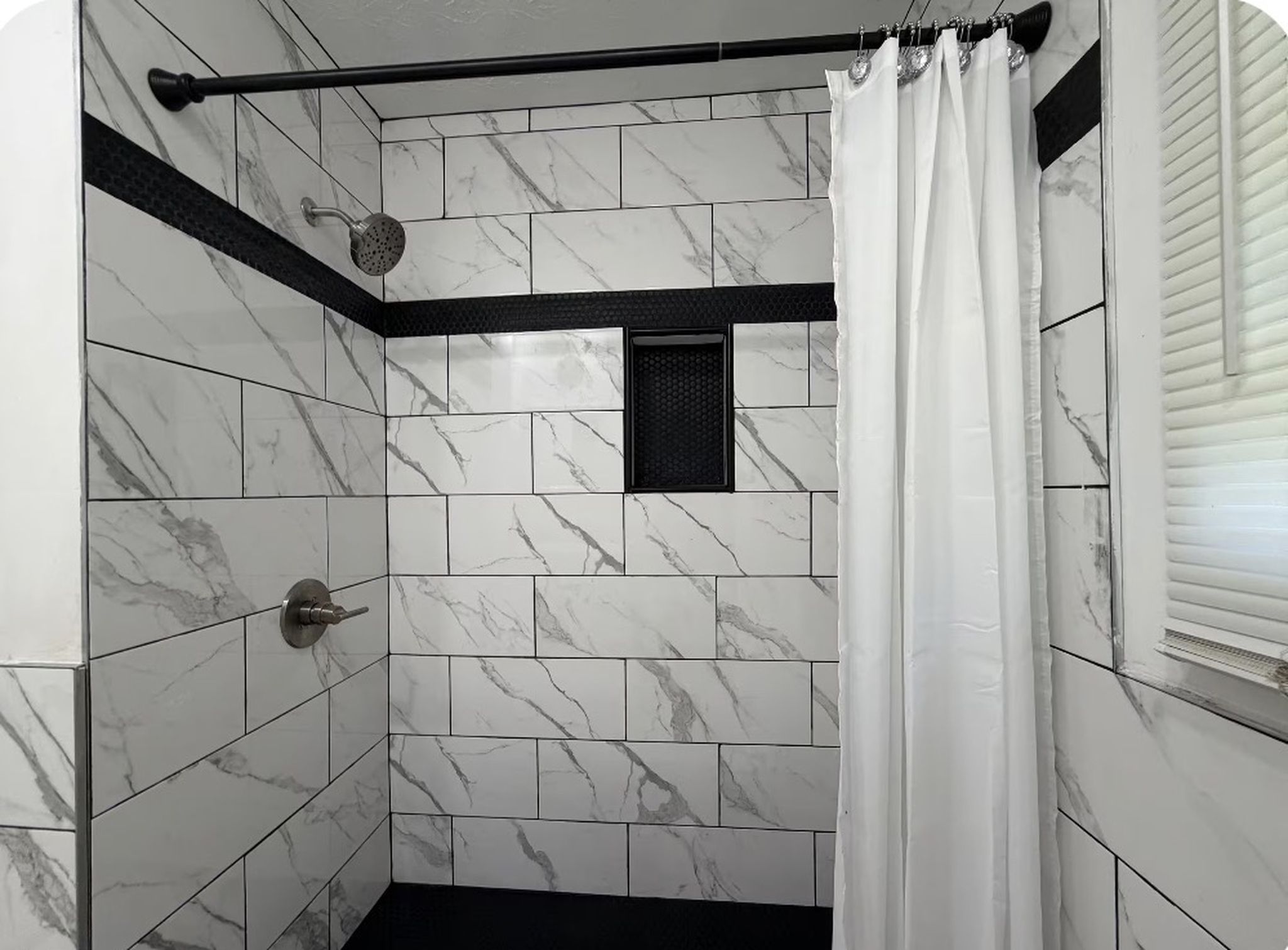 A shower area with white marble tiles, a showerhead, and a curtain.