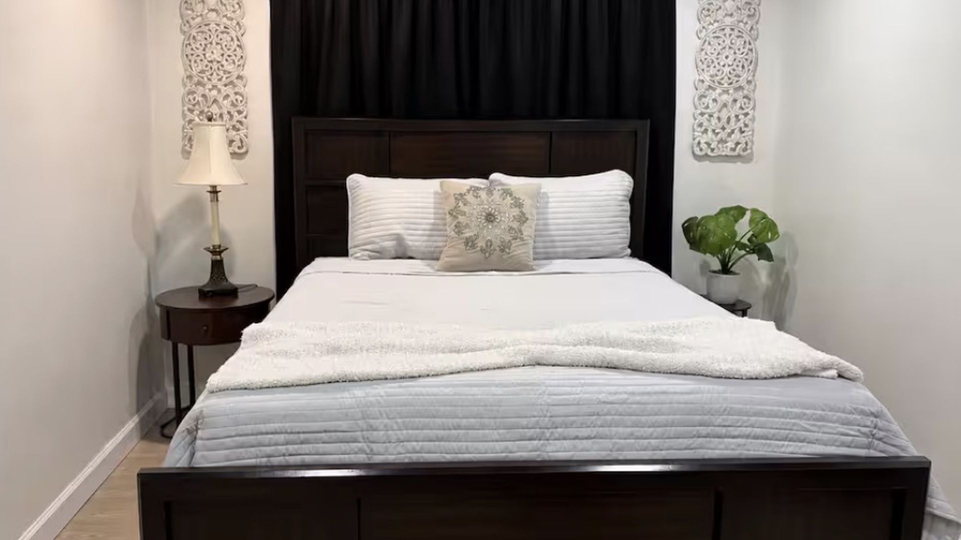 Un lit bien fait, avec une couette blanche et des oreillers, une table de chevet avec une lampe et un élément décoratif mural.