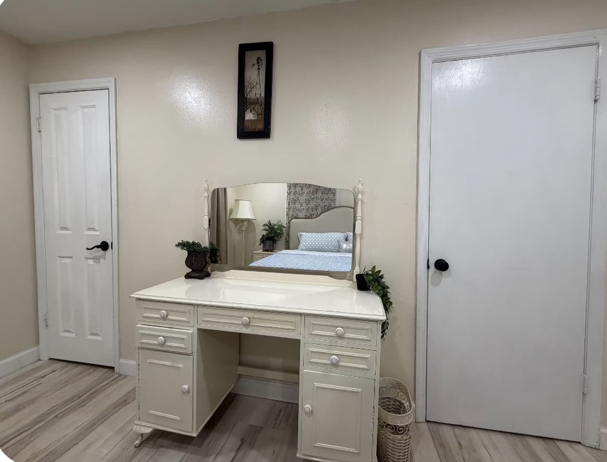 Una camera da letto con una cassettiera bianca, un letto con copriletto decorato, una lampada da comodino e un quadro appeso al muro.