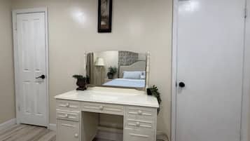 Una camera da letto con una cassettiera bianca, un letto con copriletto decorato, una lampada da comodino e un quadro appeso al muro.