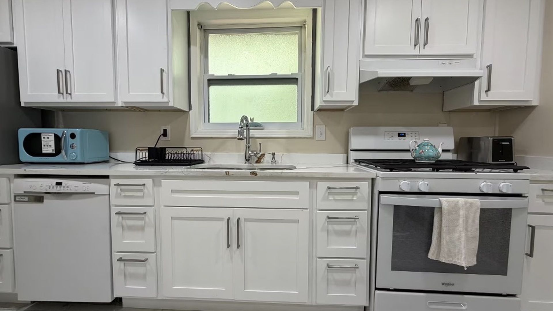 Et køkken med hvide skabe, en mikrobølgeovn, en komfur og en vask.