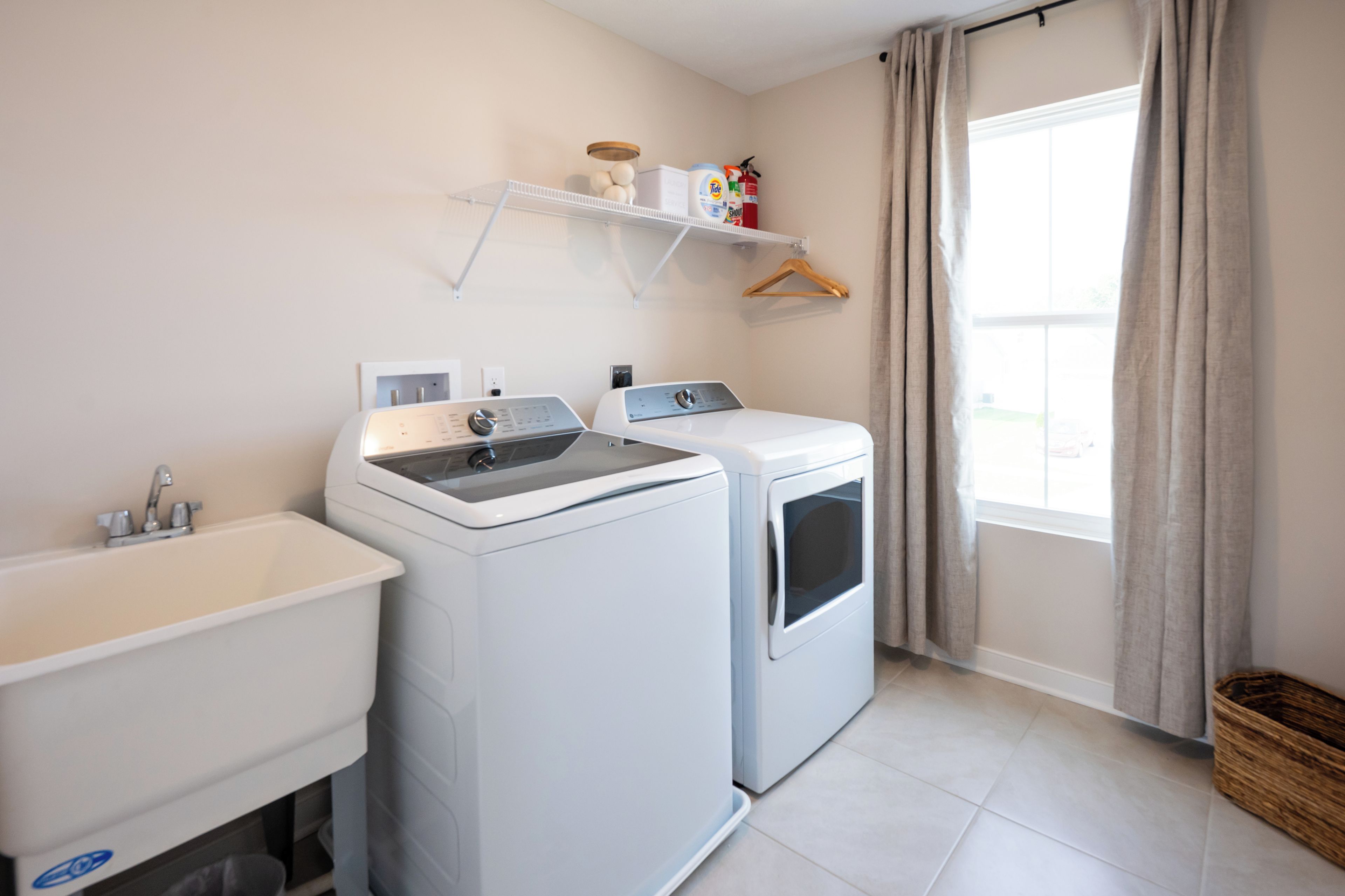 A laundry room with two washing machines, a sink, and a shelf with laundry supplies.