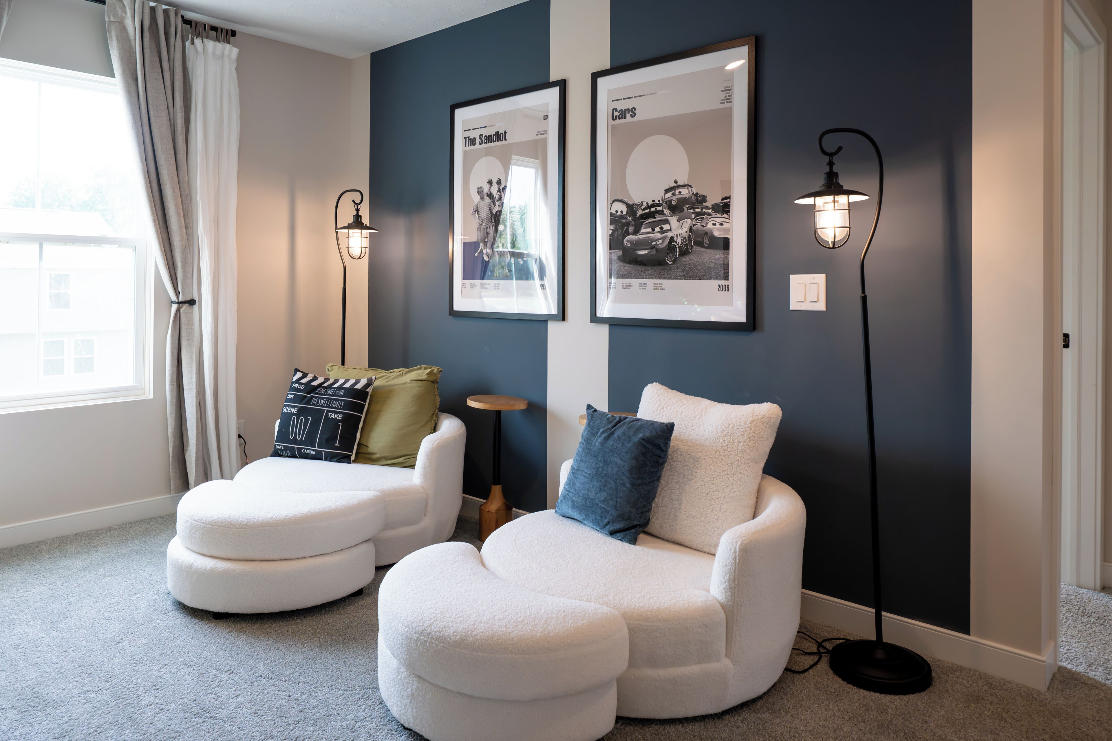 A modern living room with two white armchairs, a floor lamp, and two framed posters on the wall.