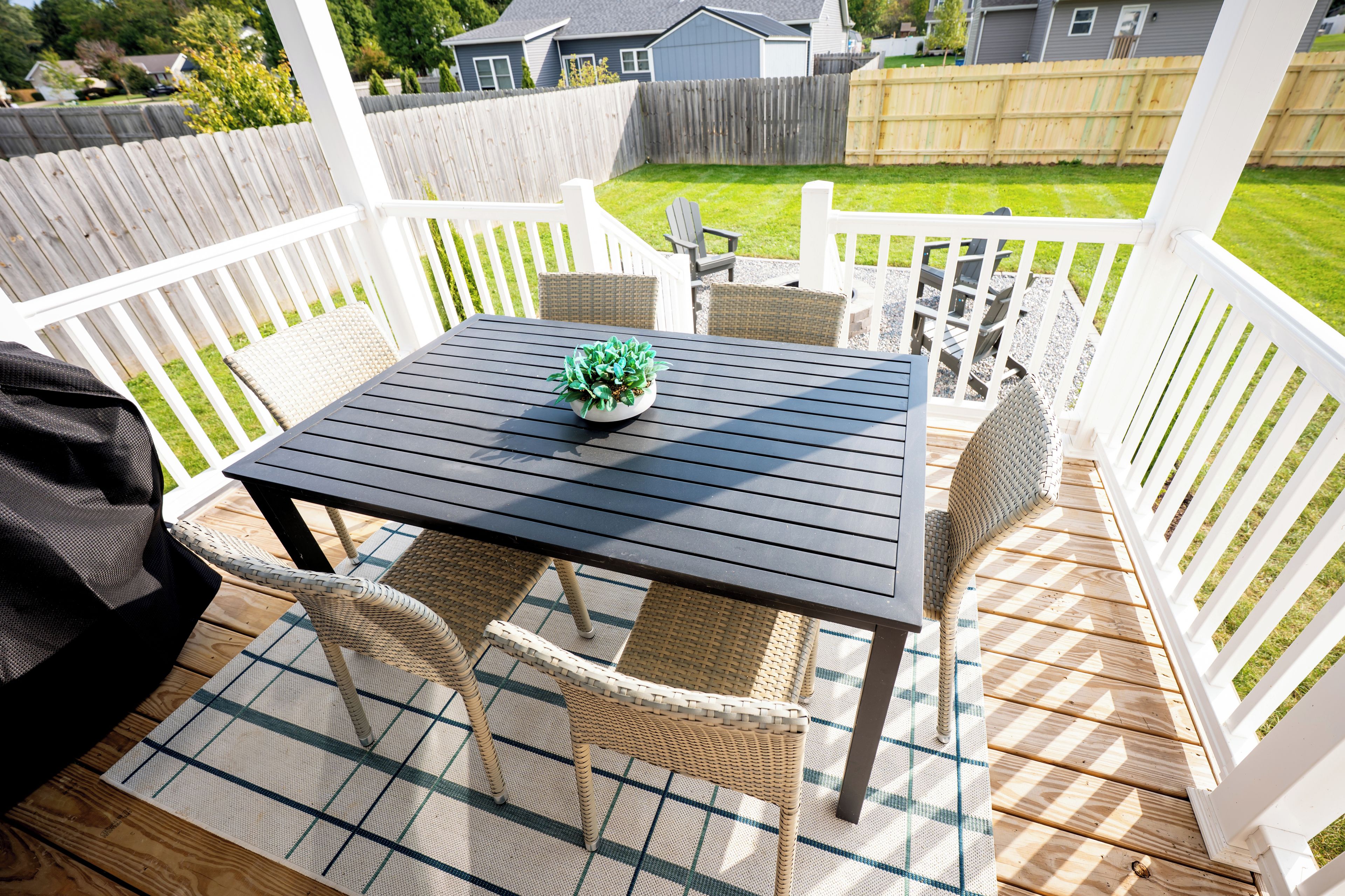 Une terrasse extérieure couverte, avec une table et des chaises, un pot de fleurs et une vue sur un jardin.