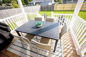 A covered outdoor patio with a table and chairs, a potted plant, and a view of a backyard.