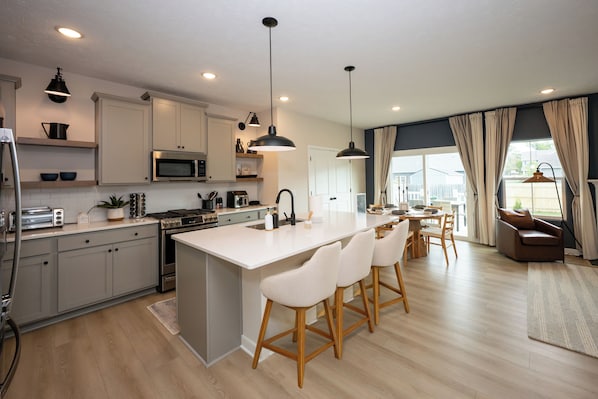 A modern kitchen with a central island, bar stools, and a dining area with a view.