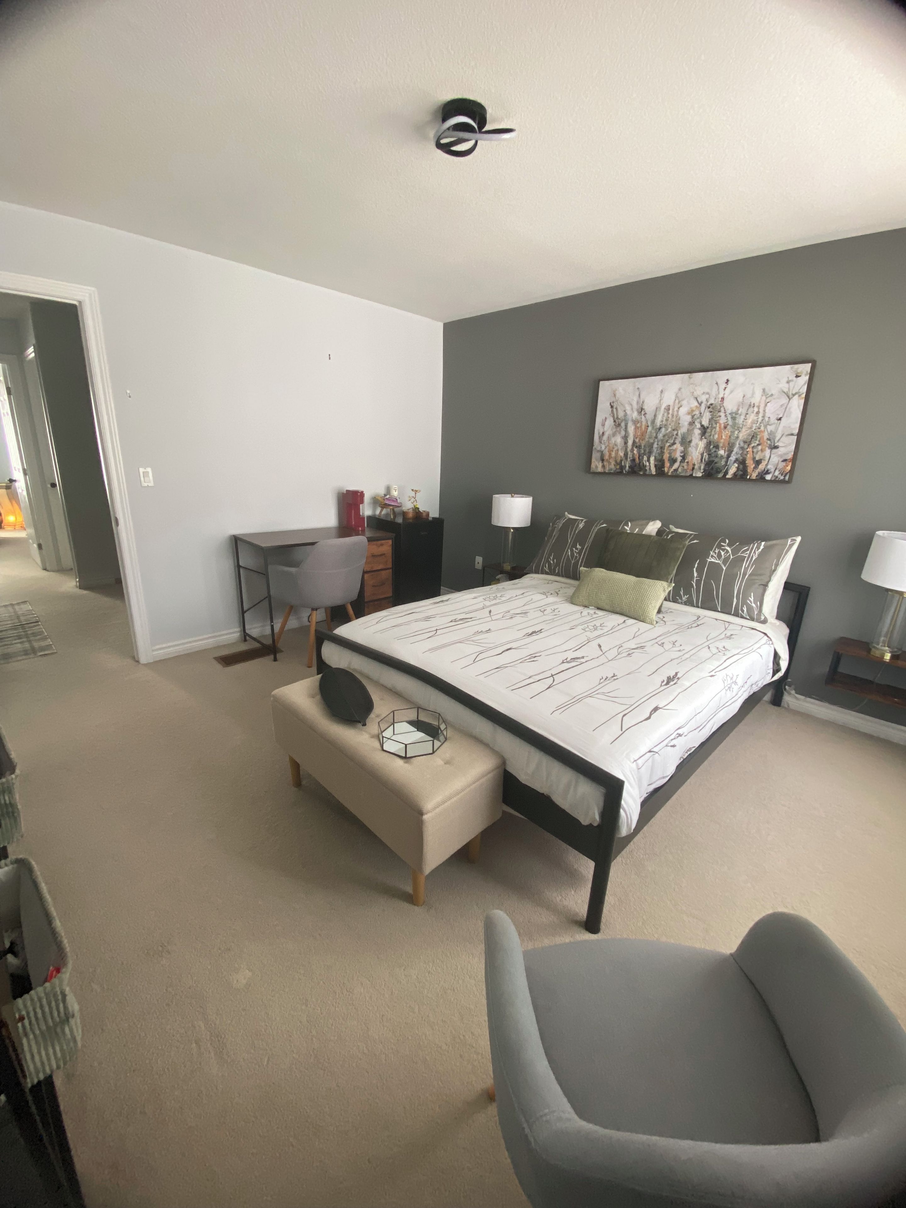A bedroom with a bed, a desk, a chair, and a painting on the wall.