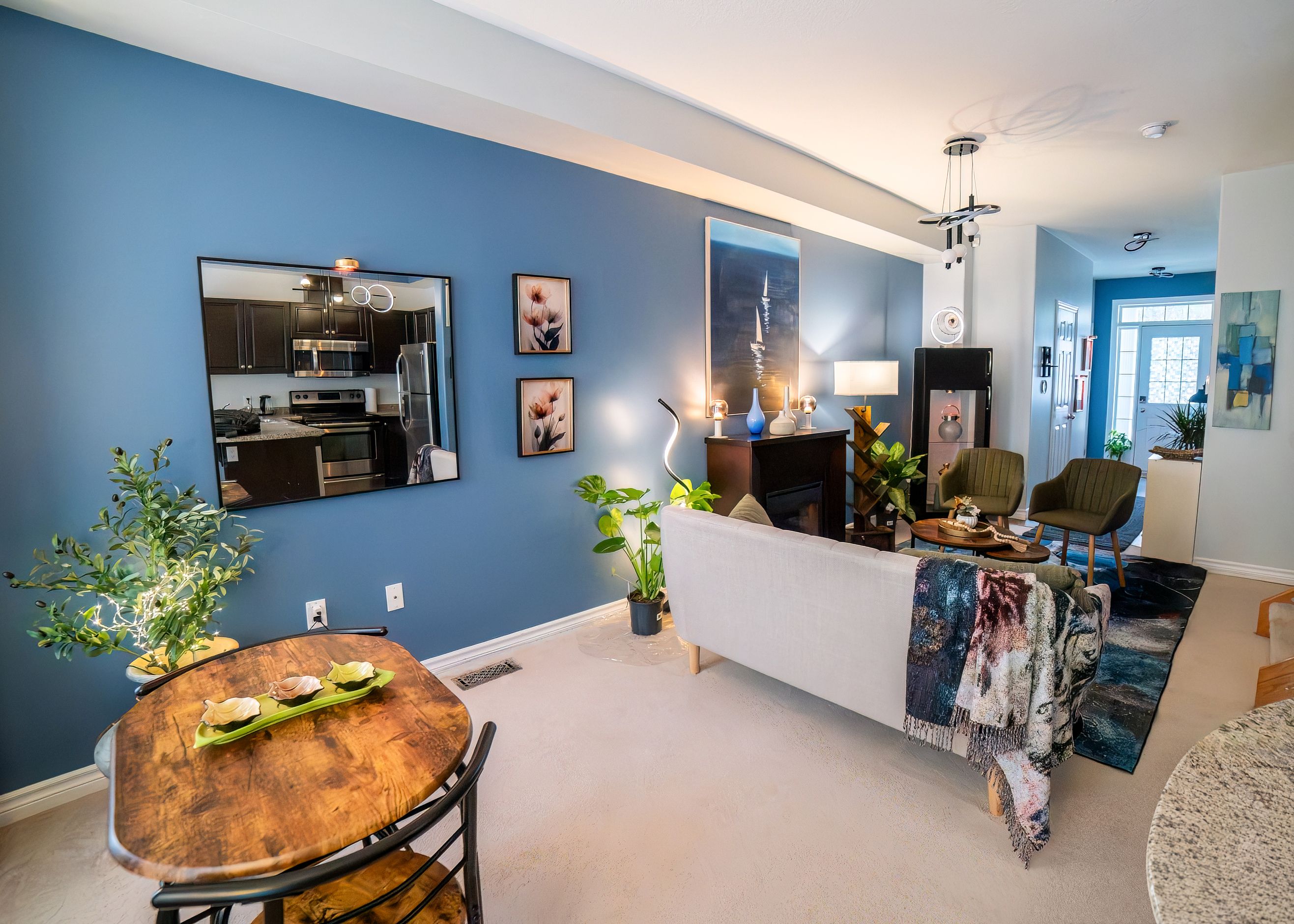 A modern living room with a blue wall, a dining area with a wooden table, and a kitchen visible through a large mirror.