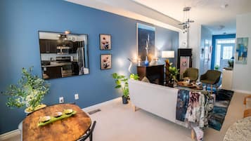 A modern living room with a blue wall, a dining area with a wooden table, and a kitchen visible through a large mirror.