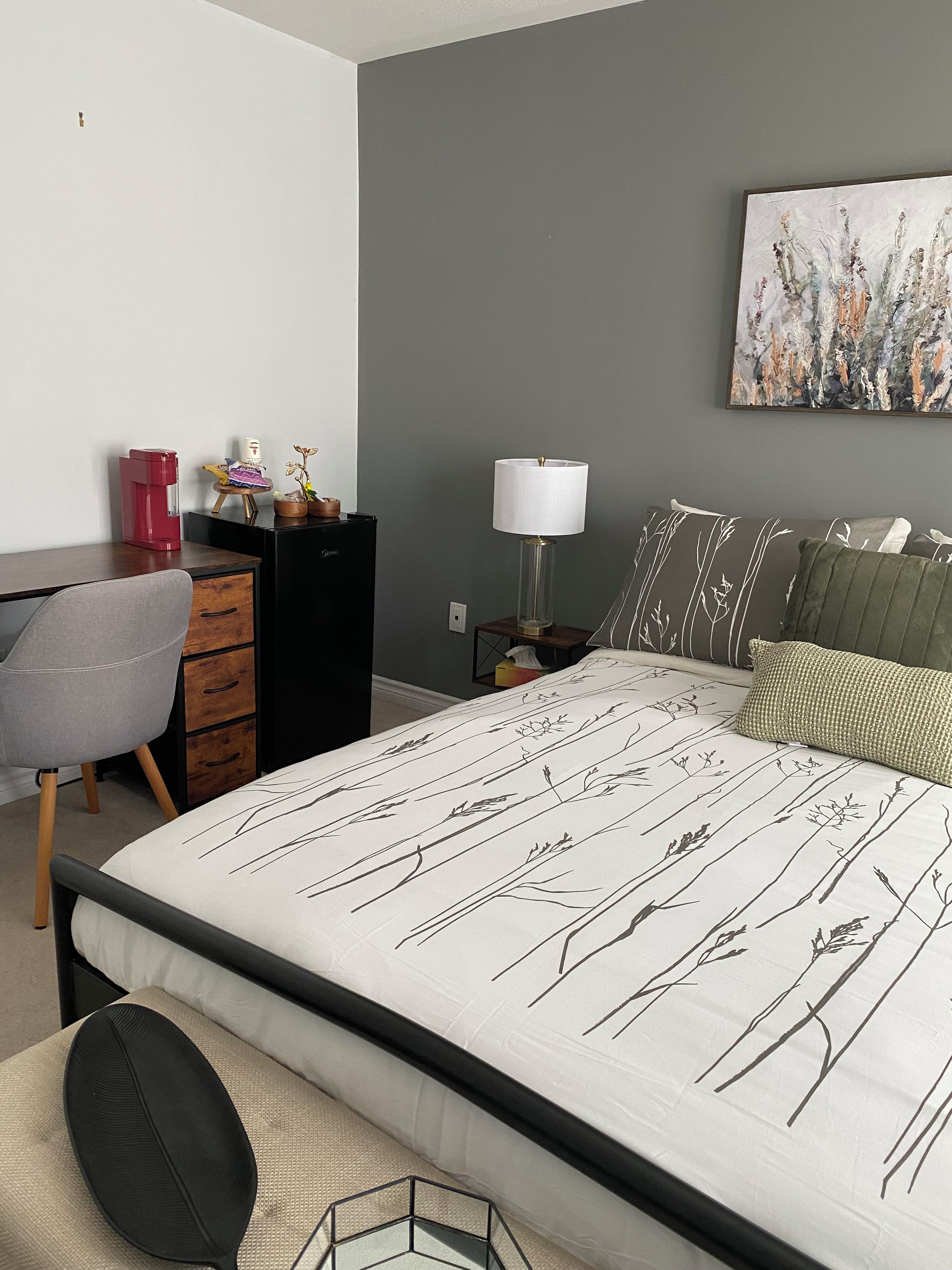 Een slaapkamer met een bed, bureau, stoel, nachtkastje en een lamp.