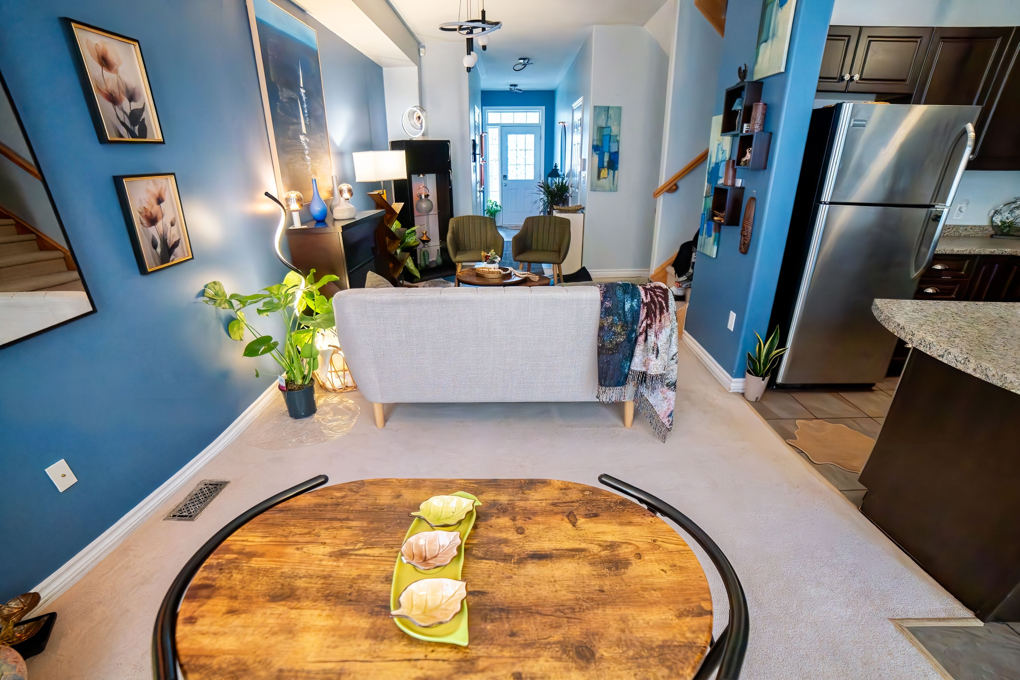 A modern kitchen with a built-in refrigerator, a dining area with a round wooden table, and a living room with a sofa and chairs.