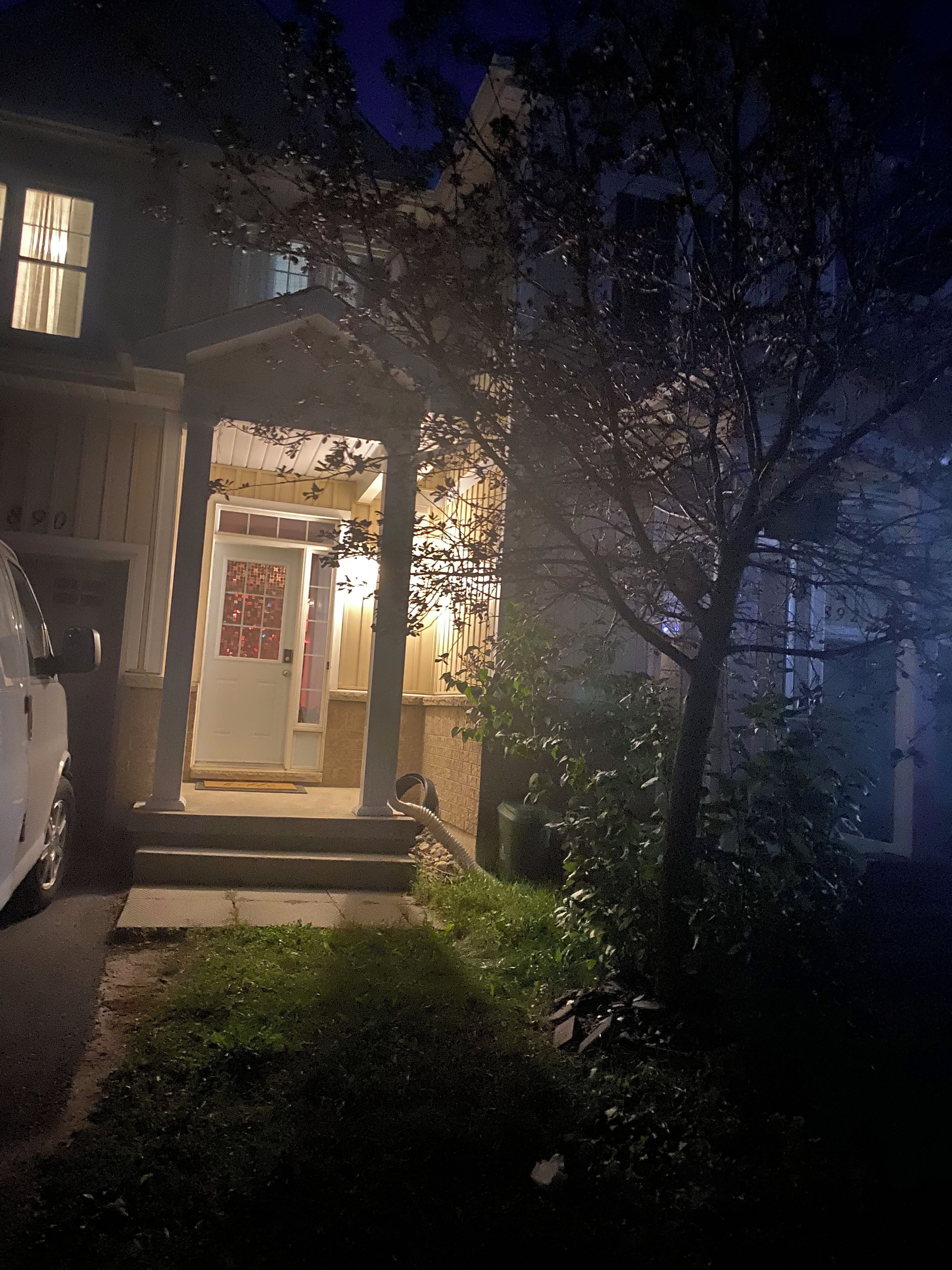 Un immeuble résidentiel avec un porche à l’avant, une porte bien visible et un véhicule garé sur le côté gauche.