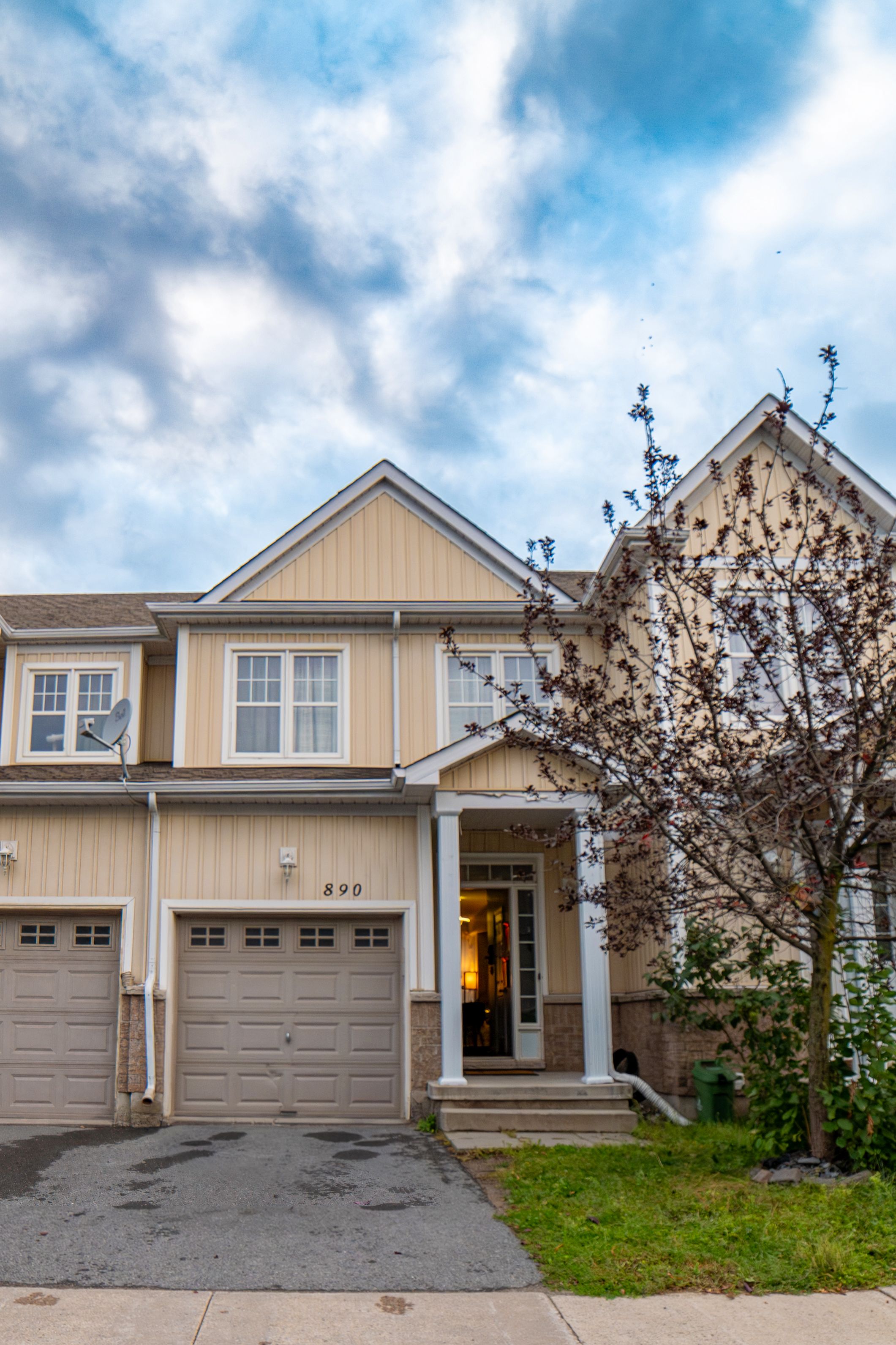 A two-story residential house with a garage, a covered porch, and a tree in the front yard.