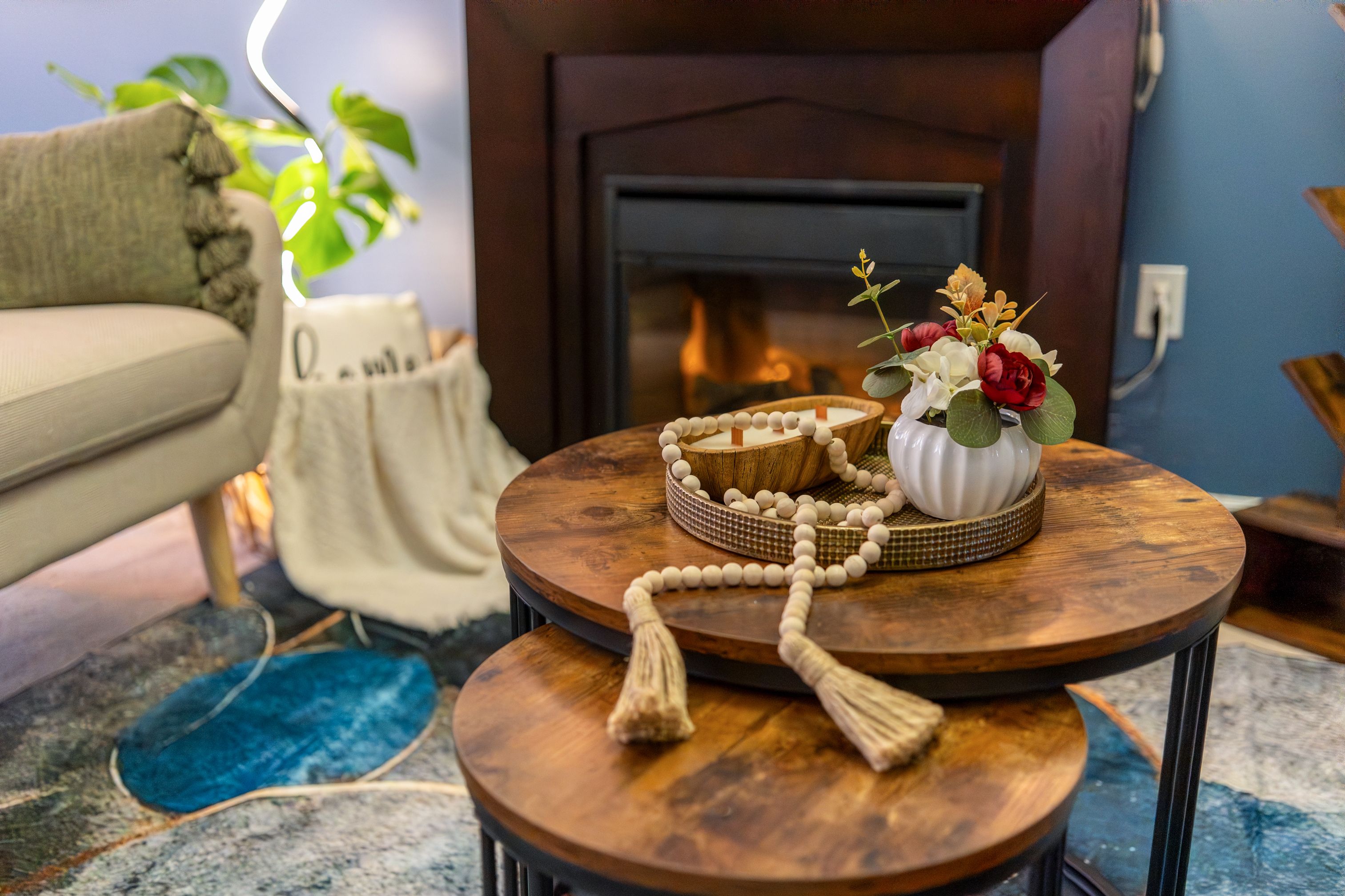 A cozy living room with a round wooden coffee table, a white vase with flowers, and a prayer bead necklace.