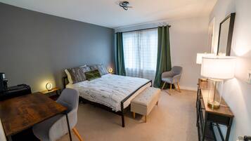 A hotel room with a bed, a desk, a chair, a bench, a dresser, and a mirror.