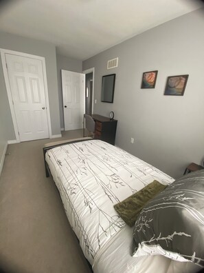 A bedroom with a bed, a desk, and two paintings on the wall.