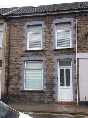 A two-story building with a stone facade, a white door, and two windows with shutters. - House Sleeps 6 (Porth)