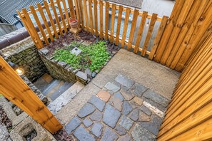 A wooden deck with a stone pathway leading to a small garden area with plants and a wooden bench.