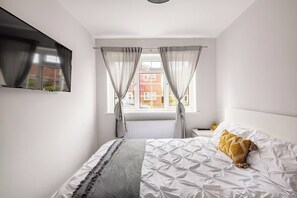 Ein Schlafzimmer mit Bett, Vorhängen, einem Fenster und einem Fernseher an der Wand.