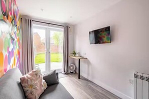 Ein modernes Wohnzimmer mit einem grauen Sofa, einem flachbildfernseher an der Wand und einer Glastür, die in einen Garten führt.