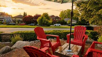 A patio with red Adirondack chairs, a wooden table, and a large umbrella.