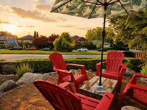 A patio with red Adirondack chairs, a wooden table, and a large umbrella. - The Maris l Lower Lonsdale Suite l Central & Cozy (North Vancouver)