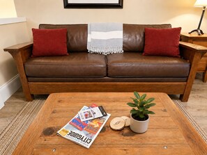 A brown leather sofa with red cushions, a wooden coffee table with a magazine, a potted plant, and wooden coasters. - The Maris l Lower Lonsdale Suite l Central & Cozy (North Vancouver)