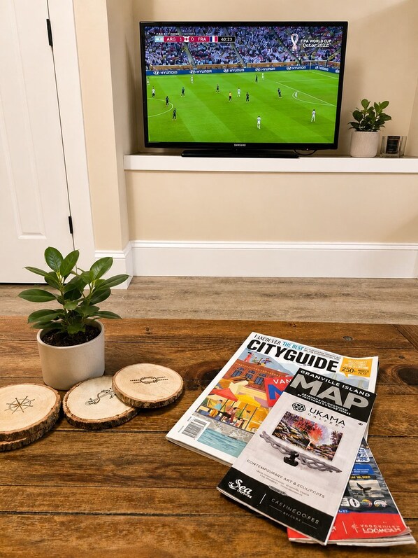 A television displaying a sports event, a magazine on a wooden surface, and a potted plant.