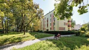 A residential building with multiple floors, a paved walkway, and a person sitting on a bench. - Astronautów Chopin Airport Apartment (Warszawa)