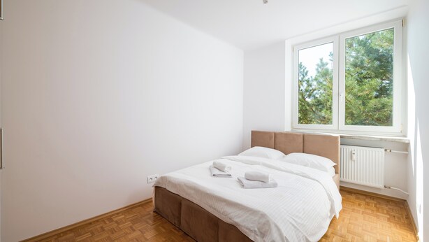 A bedroom with a bed, a window, and a radiator. - Astronautów Chopin Airport Apartment (Warszawa)