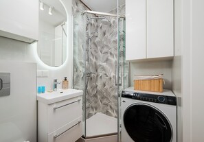 Ein modernes Badezimmer mit Duschkabine aus Glas, einer integrierten Waschmaschine und einem Waschtisch mit Spiegel.