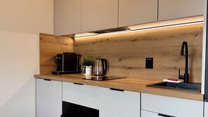 A modern kitchen with a built-in oven, a coffee maker, a kettle, and a sink with a faucet. - Nyska Boutique Studio (Wrocław)