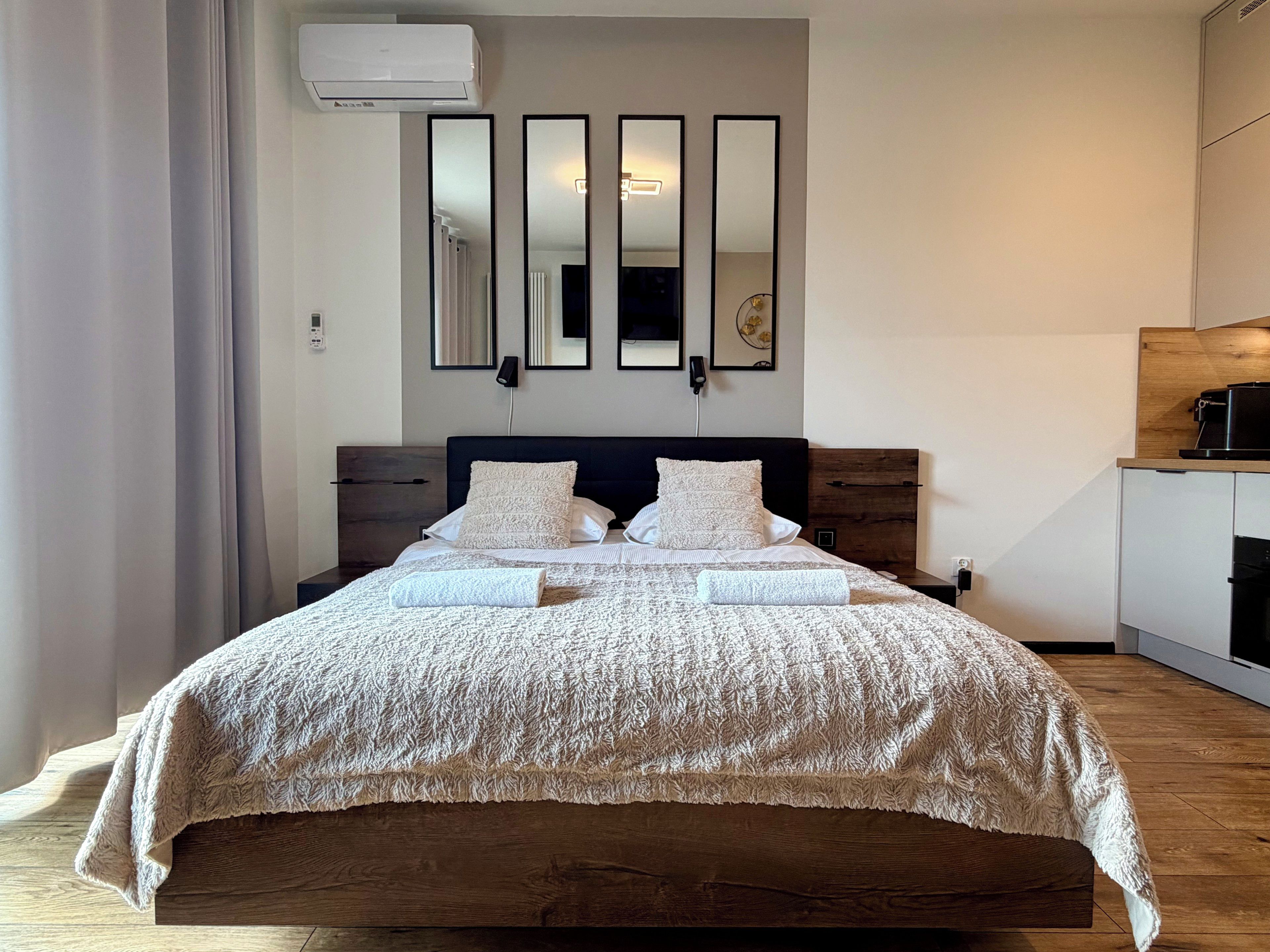 Un dormitorio moderno con una cama grande, un cabecero de madera, un escritorio empotrado y un aire acondicionado de pared.