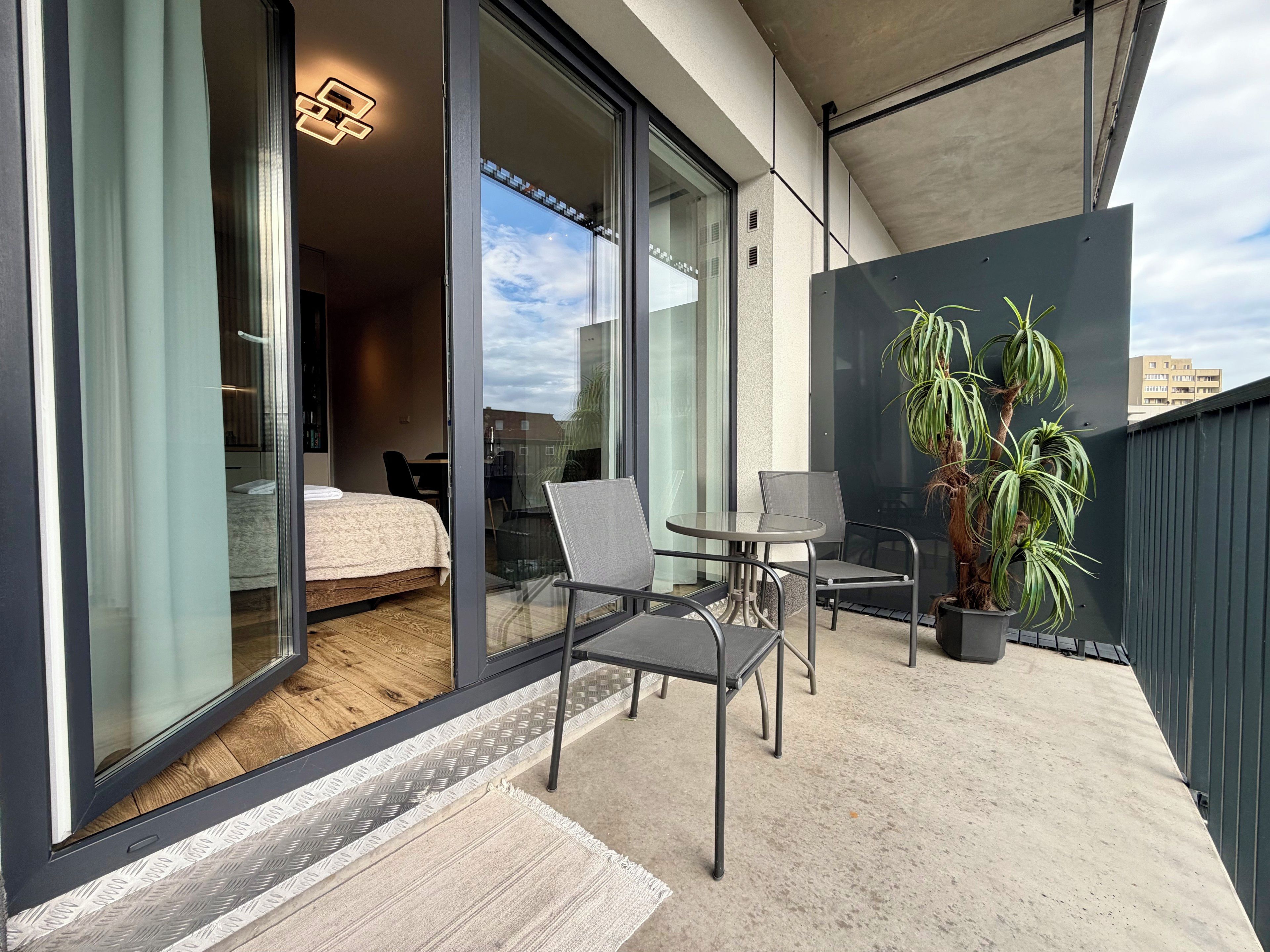 Een balkon met een bed, een tafel, stoelen en een plant in een pot.