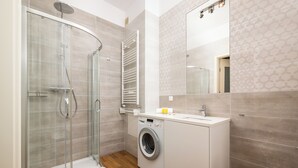 Un bagno moderno con doccia vetrata, lavatrice integrata e uno specchio grande.
