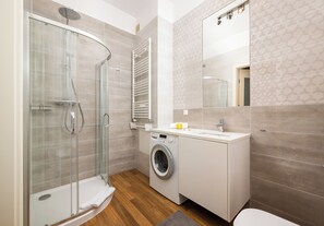 A modern bathroom with a glass-enclosed shower, a built-in washing machine, and a large mirror. - Metro Politechnika Spacious Apartment (Warszawa)